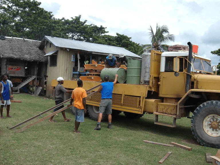 Friends In Action Intl. members and natives working on loading barrels onto a construction vehicle.