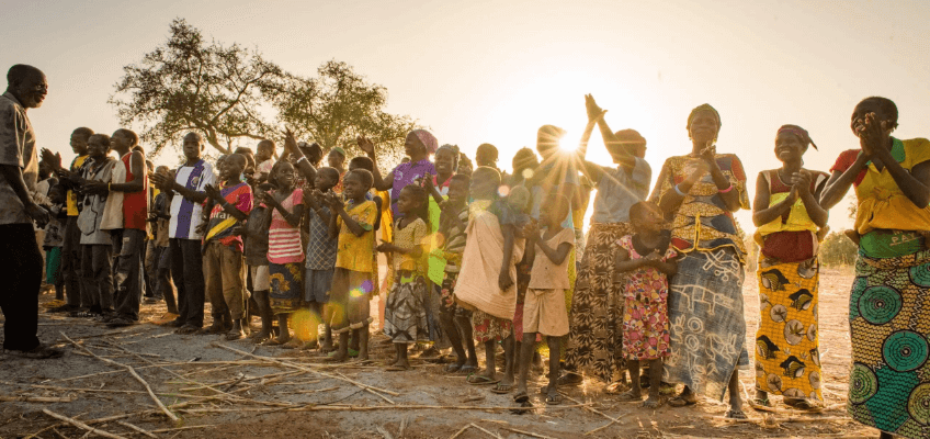 People in smiling and clapping as the sun is setting behind them.