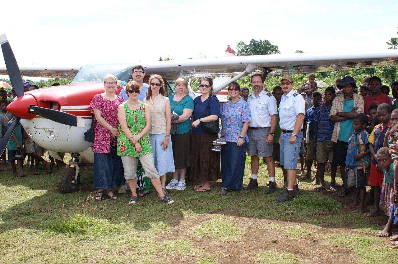 An image of FIA team and volunteers with villagers next to a airplane.